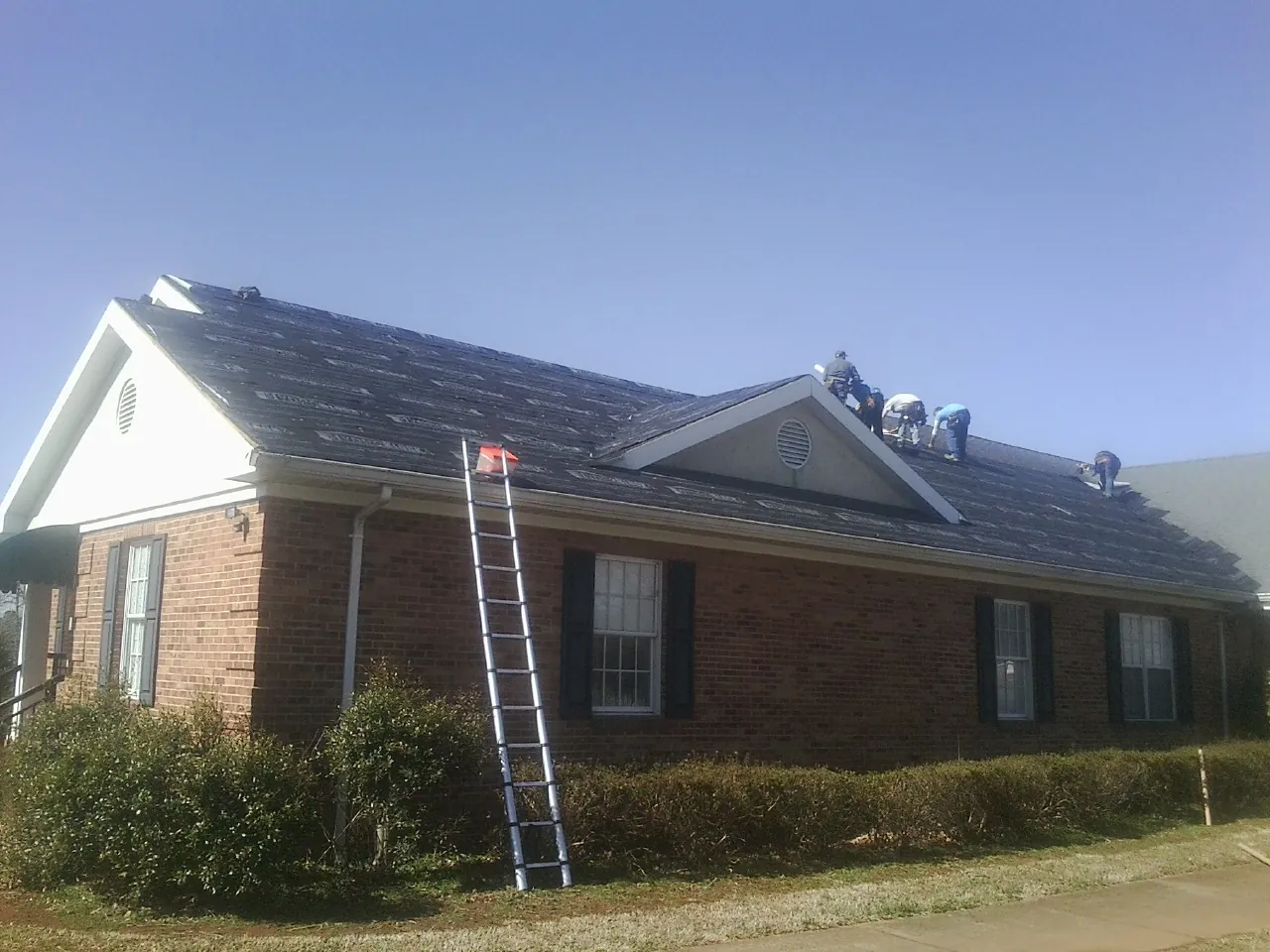 Crew tearing shingles off a brick ranch roof with a ladder set — Emergency Roof Repair work by our crew in Harvey