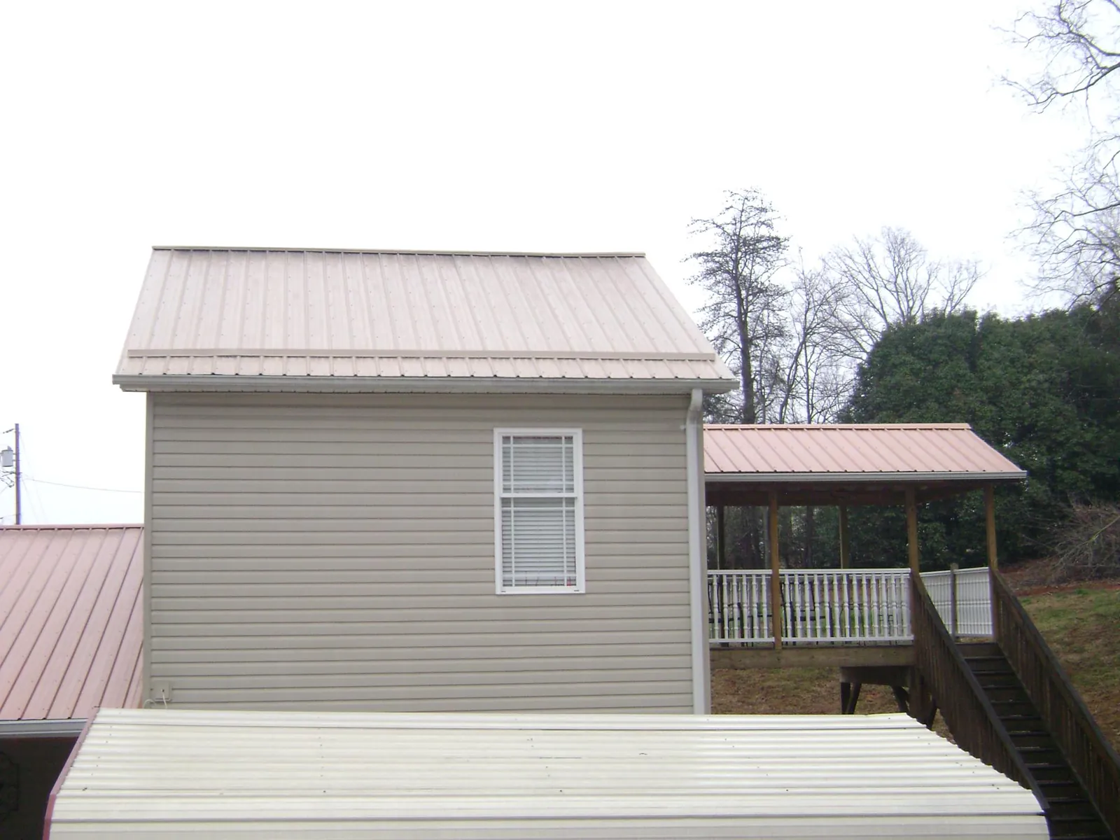 Tan metal roofs on a two story addition and attached porch, from a Roof Replacement job in Harvey